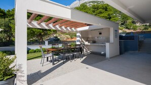 An outdoor kitchen area with a table and chairs, a grill, and a view of a mountainous landscape. - Amazing Apartment in Baska Voda With Wifi, Outdoor Swimming Pool and Heated Swimming Pool (Baska Voda)