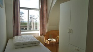 Een kamer met een bed, een rieten stoel, een kledingkast en een raam met gordijnen.