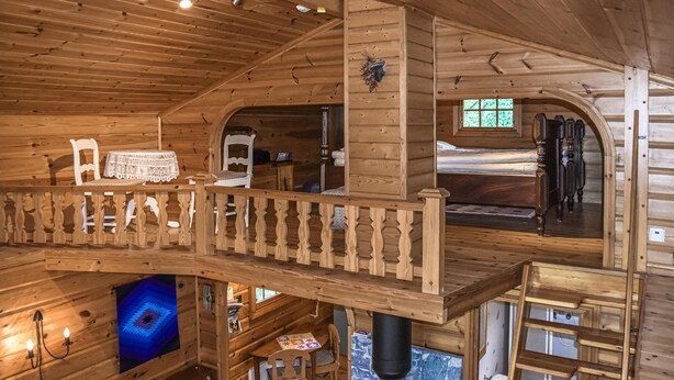 A wooden cabin interior with a loft bedroom, a dining area, and a kitchen.