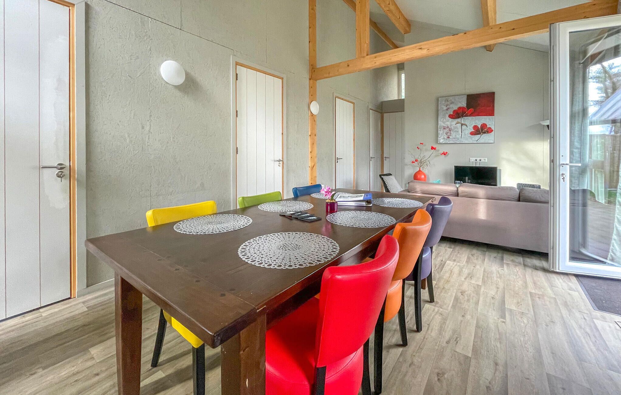 Ein Essbereich mit einem Holztisch, bunten Stühlen und einer modernen Küche im Hintergrund.