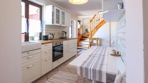 Een keuken met witte kasten, een houten trap en een eethoek met een tafel en stoelen.