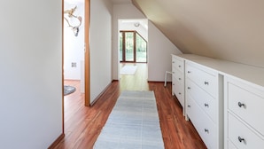 Een ruime gang met houten vloeren, een witte ladekast en een vloerkleed.