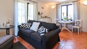 Een woonkamer met een bank, een klein tafeltje en een eethoek met stoelen.