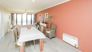 A dining area with a long table, chairs, a radiator, and a window with curtains. - Amazing Apartment in Oostende With Wifi and 1 Bedrooms (Ostend)