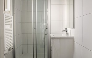 A modern bathroom with a glass shower enclosure, a white sink with a chrome faucet, and a white radiator.