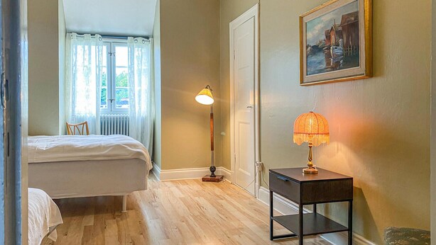 Un dormitorio con una cama, una lámpara de pie, una lámpara de mesa y un cuadro en la pared.
