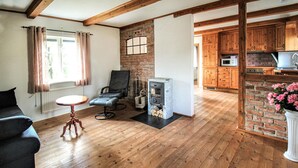 Una sala de estar acogedora con chimenea, piso de madera, una mesa de comedor y una zona de cocina con armarios de madera y pared de ladrillo.