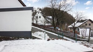 Ett snötäckt bostadsområde med en vit byggnad, ett trästaket och en kulle med ett hus på toppen.