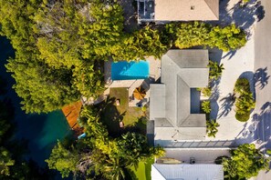 Vue aérienne d’une propriété résidentielle dotée d’une piscine, d’une cour clôturée et entourée d’arbres.