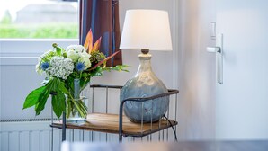 Et værelse med et vindue, en lampe på en hylde og en vase med blomster.
