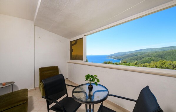 A balcony with a table and chairs, a potted plant, and a view of a coastal landscape.