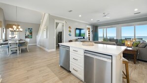 A spacious kitchen with a central island, a dining area with a table and chairs, and a living area with a sofa and a view of the ocean.