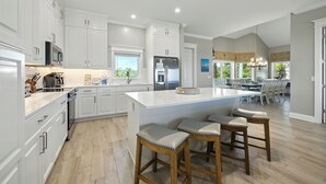 A spacious kitchen with white cabinetry, a large island with bar stools, and a view to the dining area.