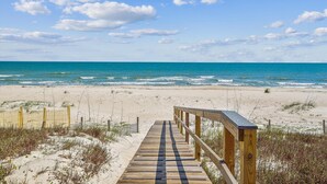 A wooden boardwalk leading to a sandy beach with a clear view of the ocean.