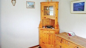 A wooden cabinet with a glass door, a framed picture on the wall, and a cup on a wooden dresser. - Amazing Home in Färjestaden With 1 Bedrooms (Farjestaden)