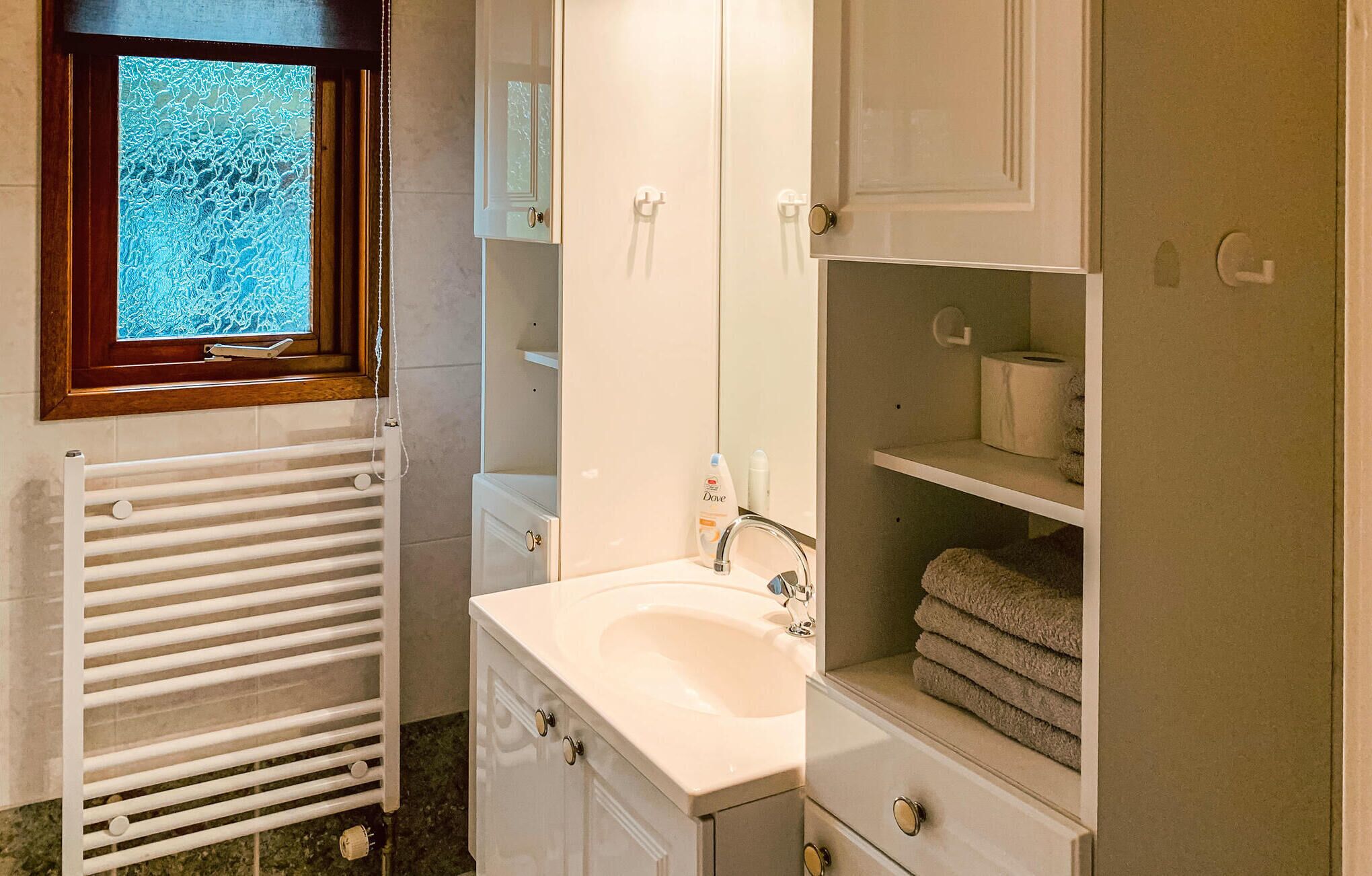 A bathroom with a white sink, a mirror, a towel rack, and a window with a view of trees.