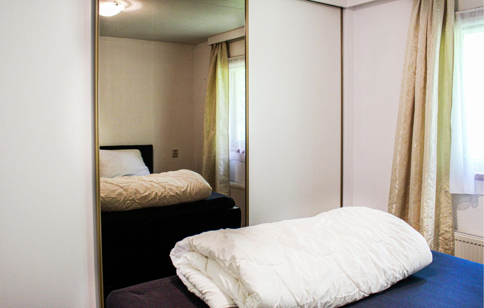 A bedroom with a bed, a mirror, and a window with curtains.