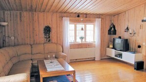 A cozy living room with a wooden ceiling, a sofa, a coffee table with a placemat, a television on a stand, and a window with curtains.