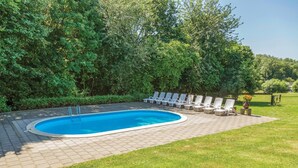 A swimming pool with a paved deck, surrounded by lush greenery and a row of white lounge chairs. - Vakantiewoning 11 (Simpelveld)