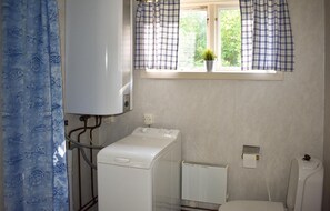 A bathroom with a white heater, a white washing machine, and a window with a plant on the sill. - Amazing Apartment in Rönneshytta With 1 Bedrooms (Rönneshytta)