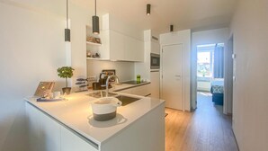 Una cucina moderna con mobili bianchi, un'isola centrale, illuminazione a sospensione e vista su un balcone.