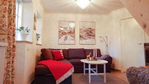 A cozy living room with a brown sofa, a red throw blanket, a small white table with decorative items, and two framed pictures on the wall. - Stunning Home in Visby With 2 Bedrooms and Wifi (Visby)