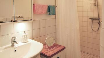 A bathroom with a white sink, a mirror, a towel rack with pink and blue towels, a shower with a handheld showerhead, and a wooden vanity.