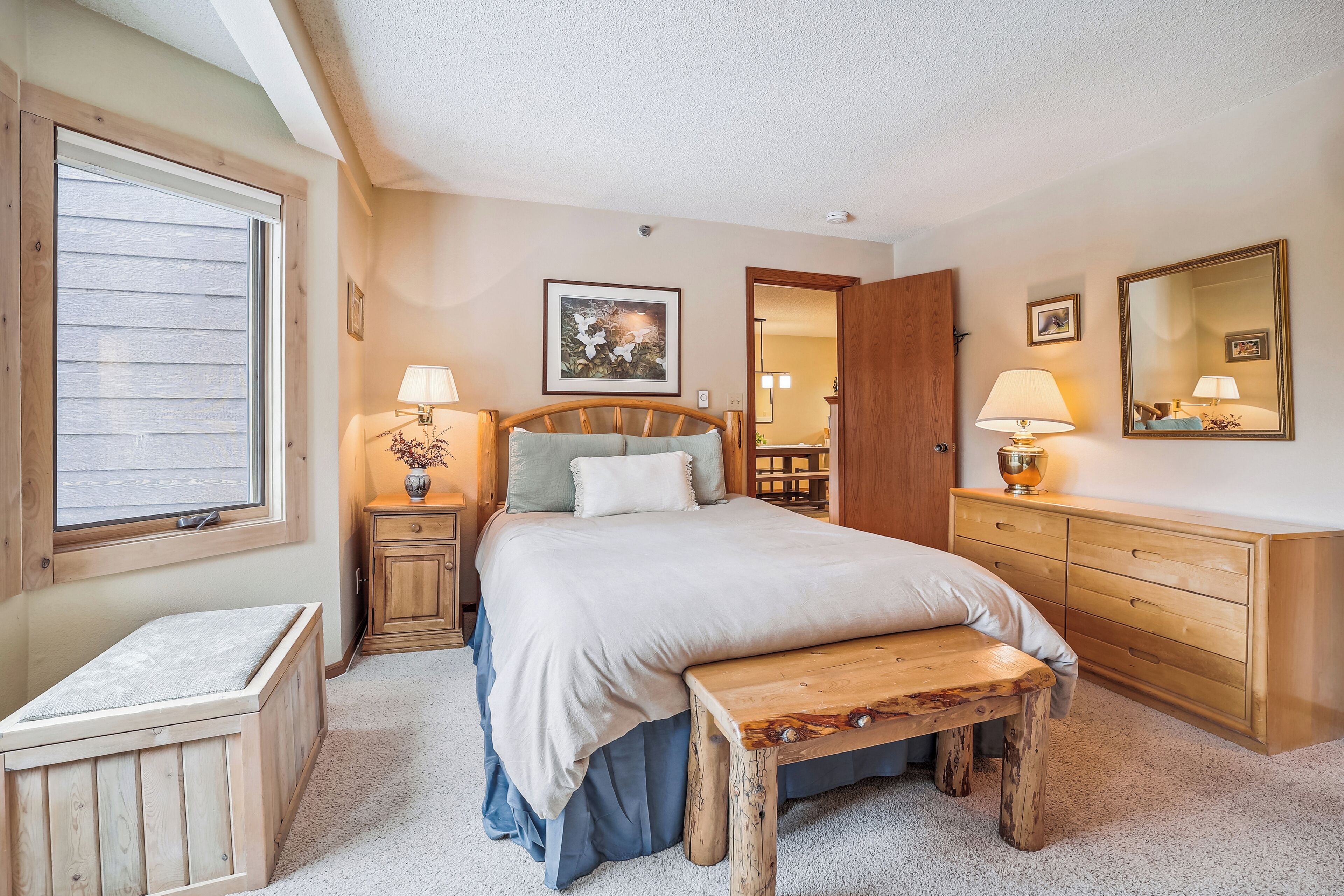A bedroom with a bed, bedside tables, a bench, a dresser, and a window.