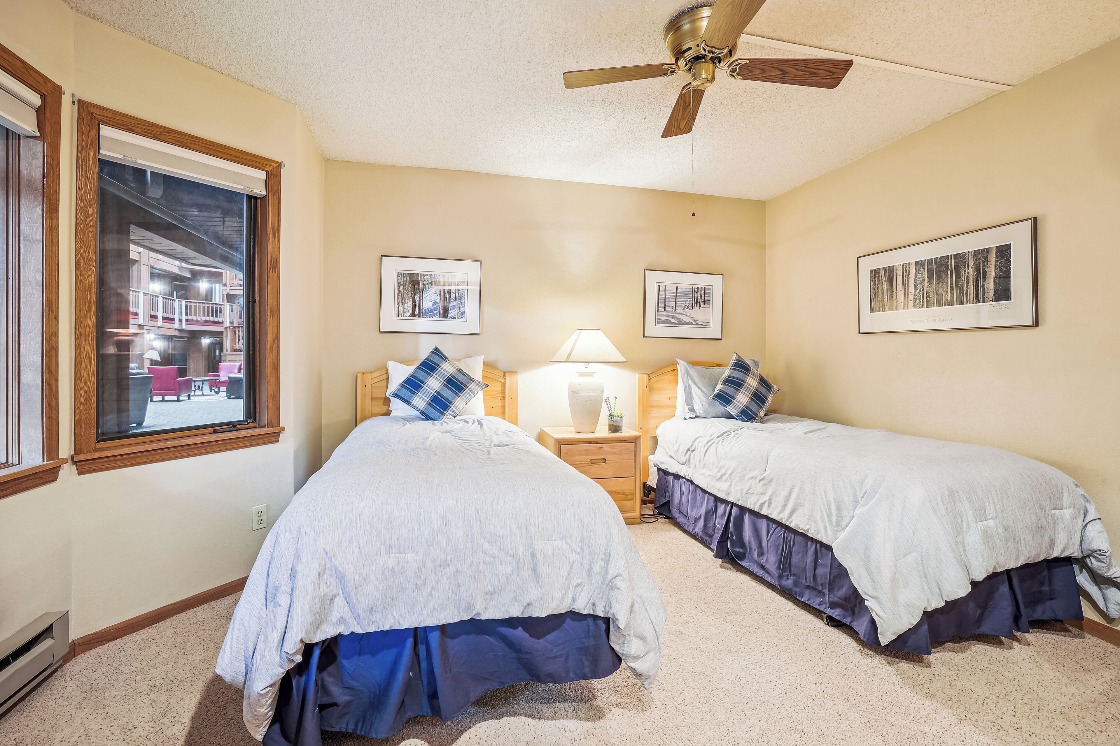 A bedroom with two beds, a ceiling fan, and framed pictures on the walls.