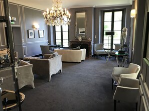 Un salon spacieux agrémenté d’un magnifique lustre, d’une cheminée et d’un grand miroir.