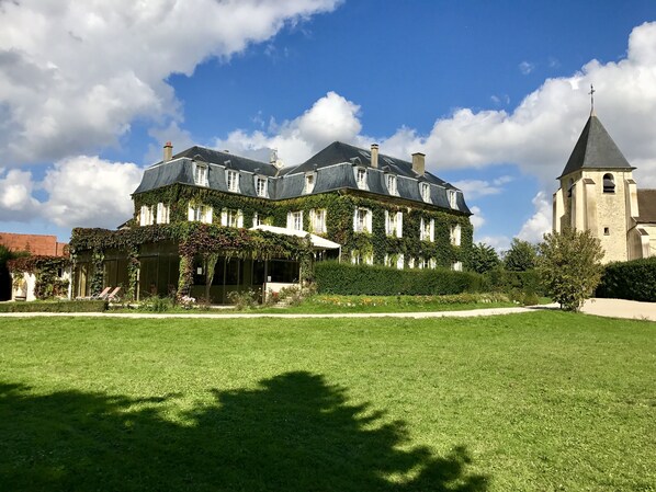 Un grand bâtiment recouvert de lierre, doté d’une tour imposante, et entouré d’une pelouse et d’un jardin bien entretenus.