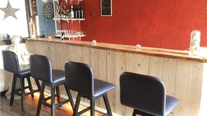 A bar area with wooden bar counter, black bar stools, and shelves with bottles and glasses.