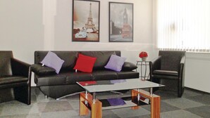 A living room with a black leather sofa, two armchairs, a glass coffee table, and two framed pictures of the Eiffel Tower and Big Ben.