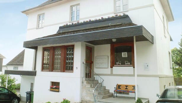 A two-story building with a white facade, a dark roof, and a small porch area with a bench.