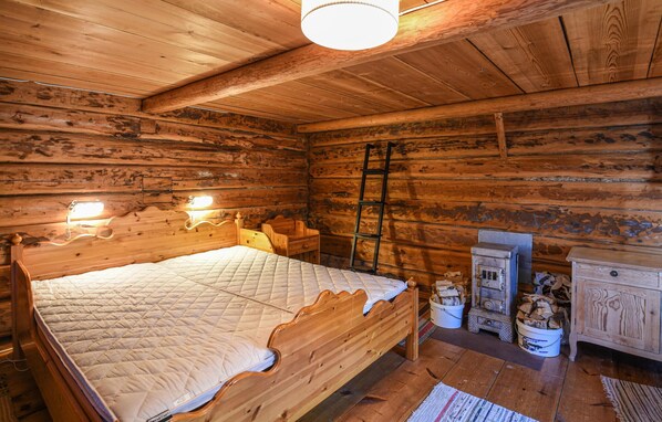 A wooden cabin bedroom with a bed, a nightstand, a dresser, a ladder, and a heater.