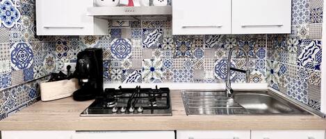 A kitchen with white cabinets, a gas stove, a sink, and decorative tiles.