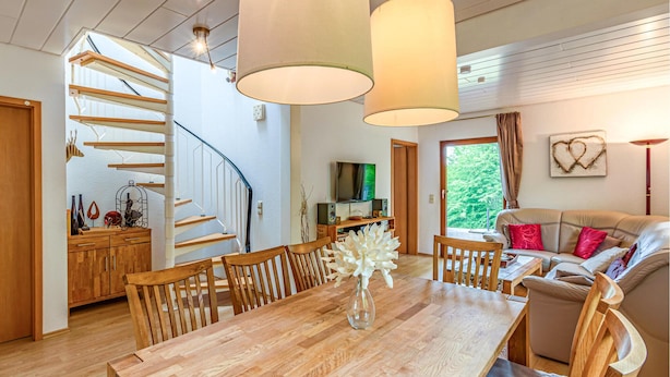 A modern interior with a wooden staircase, a dining area with a wooden table and chairs, a living room with a sofa, and a TV on a wooden stand. - Nice Home in Kirchheim With 5 Bedrooms and Wifi (Kirchheim)