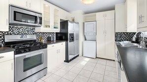 A modern kitchen with stainless steel appliances, white cabinets, and a tiled backsplash. - Holiday Pool Paradise - A Ryson Property (Palm Springs)