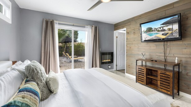 A bedroom with a bed, a TV mounted on the wall, and a fireplace. - Holiday Pool Paradise - A Ryson Property (Palm Springs)