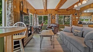 Interior acolhedor de uma cabana com área de jantar, sofá, poltrona de couro e cozinha.