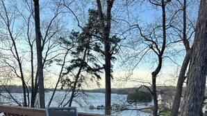 Um terraço com uma mesa redonda e cadeiras, com vista para um corpo de água e árvores.