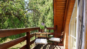 A wooden deck with two cushioned chairs and a small table with a potted plant and a lantern.