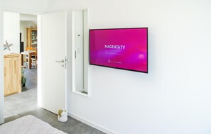 A modern room with a flat-screen TV mounted on the wall displaying 'MAGENTA TV'. - Beautiful Apartment in Büsum With 2 Bedrooms, Sauna and Wifi (Büsum)