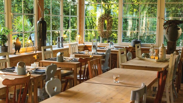 A restaurant with wooden tables and chairs, large windows with a view of greenery, and various table settings. - Vakantiewoning 10 (Simpelveld)