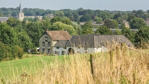 A large stone building with a prominent tower, surrounded by lush greenery and a field. - Vakantiewoning 10 (Simpelveld)