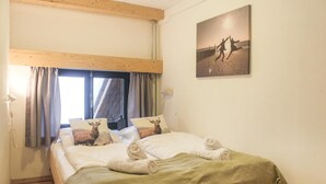 A bedroom with a bed, two pillows with deer images, a window with curtains, and a picture of two people on a beach.