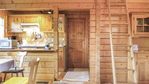 Puinen mökki, jonka sisätiloissa on keittiö, ruokapöytä tuoleineen ja puinen portaikko.