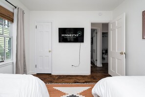 A bedroom with two beds, a TV mounted on the wall, and a view of the hallway. - MINNeSTAY* Shoreline Villa | Pool (Robbinsdale)