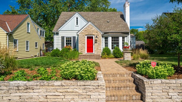 A two-story house with a red front door, stone steps leading to the entrance, and a stone wall in front. - MINNeSTAY* Shoreline Villa | Pool (Robbinsdale)