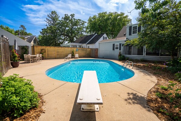 A backyard with a swimming pool, a wooden deck, and a patio area with outdoor furniture. - MINNeSTAY* Shoreline Villa | Pool (Robbinsdale)